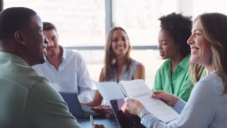 Multi-Cultural-Business-Team-Meeting-Around-Office-Boardroom-Table-With-Laptops-Discussing-Documents