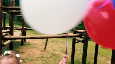 Two-girls-smiling-while-holding-balloons-in-park