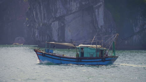 fishing boat motors out to ocean in the famous ha long bay of vietnam. a fisherman prepares the nets at the stern.
