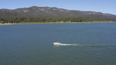 Aerial-drone-tracking-shot-of-a-white-boat-in-Big-Bear-Lake-in-San-Bernardino-County,-California