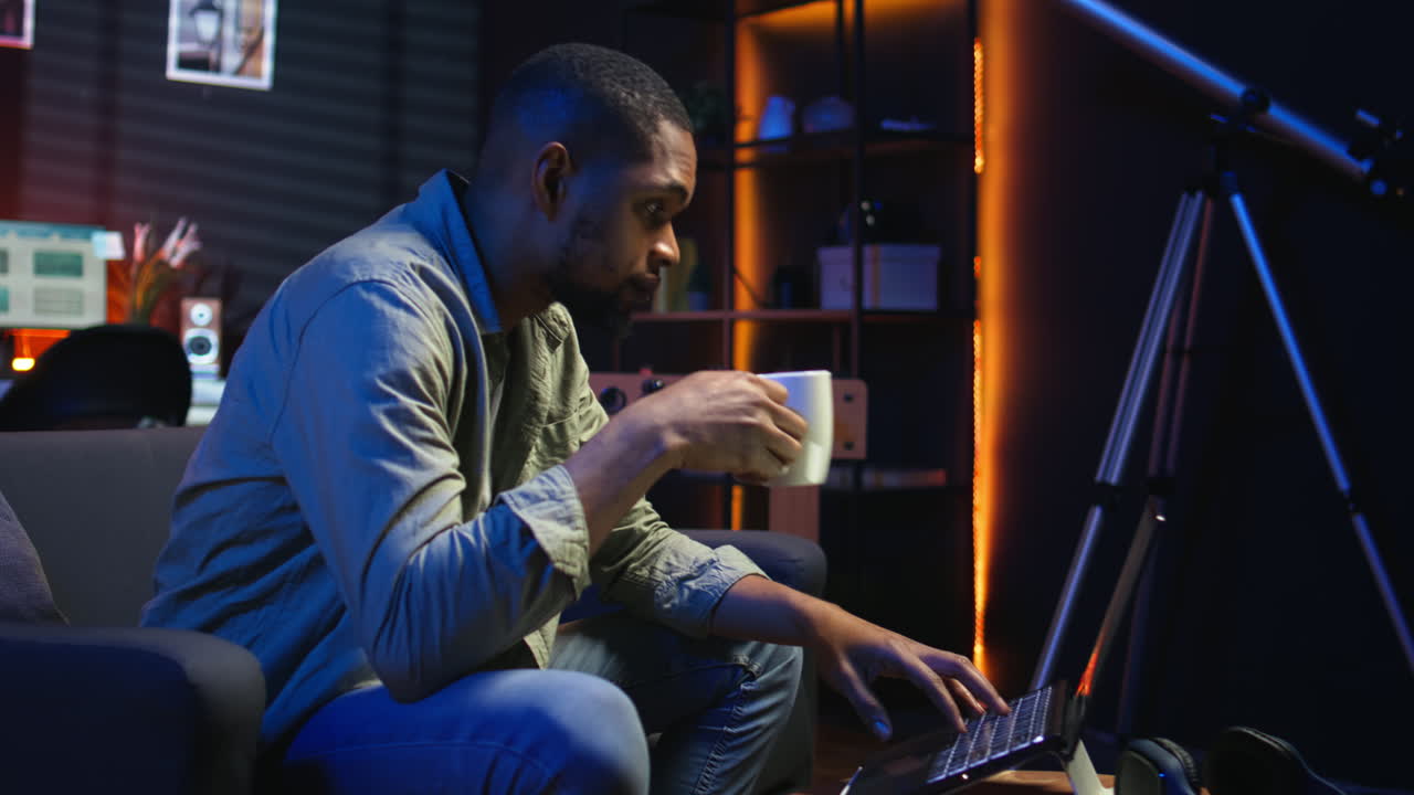 Vertical Video African American young adult working remotely on a laptop under loft neon lights