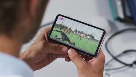 compuesto de un médico masculino viendo un partido de hockey en un teléfono inteligente