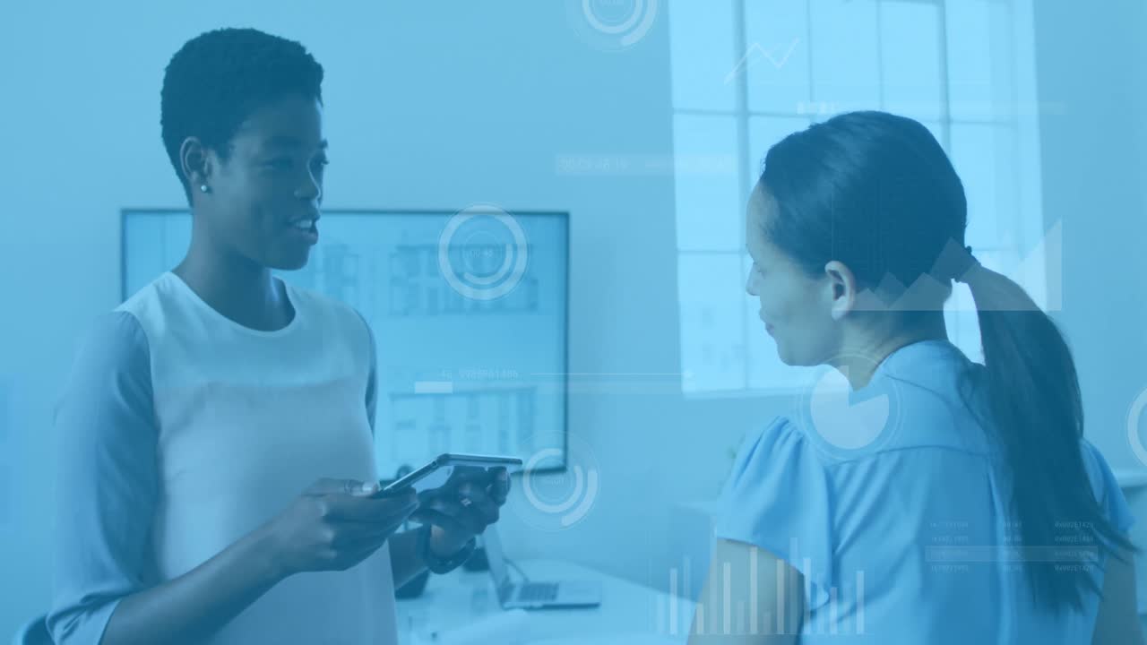 Animation of data processing over two diverse women discussing over a digital tablet at office
