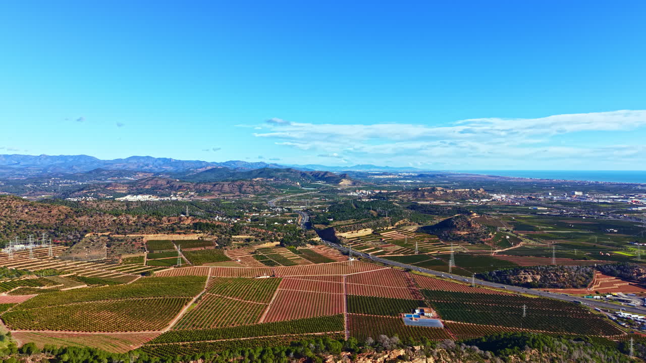 Vista di vigneti e montagne da un punto elevato della Costa Blanca con cielo blu e nuvole sparse nel pomeriggio.