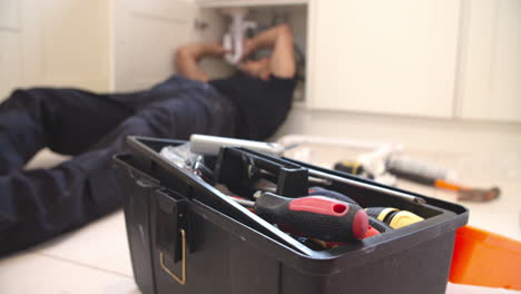 plumber fixing sink in kitchen, focus on toolbox