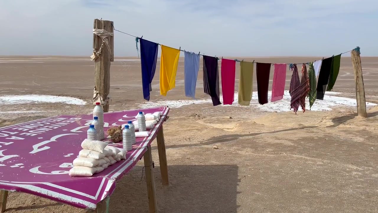 Colorful scarves hang on a line beside a simple table selling packaged salt by the dry salt lake of Chott el Djerid in Tunisia.
