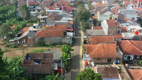 People-and-motorbikes-driving-through-a-local-neighborhood-in-Bandung-Indonesia-at-sunrise,-aerial