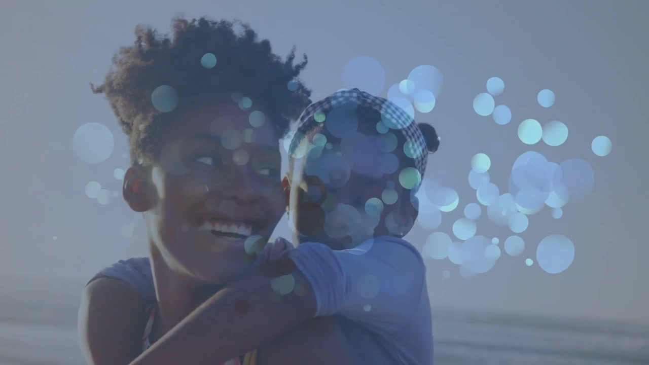 Madre che porta la figlia sulla schiena in riva al mare per un contesto lifestyle, con inquadratura ravvicinata che crea un bokeh blu sui volti.