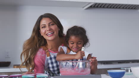 portrait of hispanic mother and daughter having fun in kitchen baking cake together