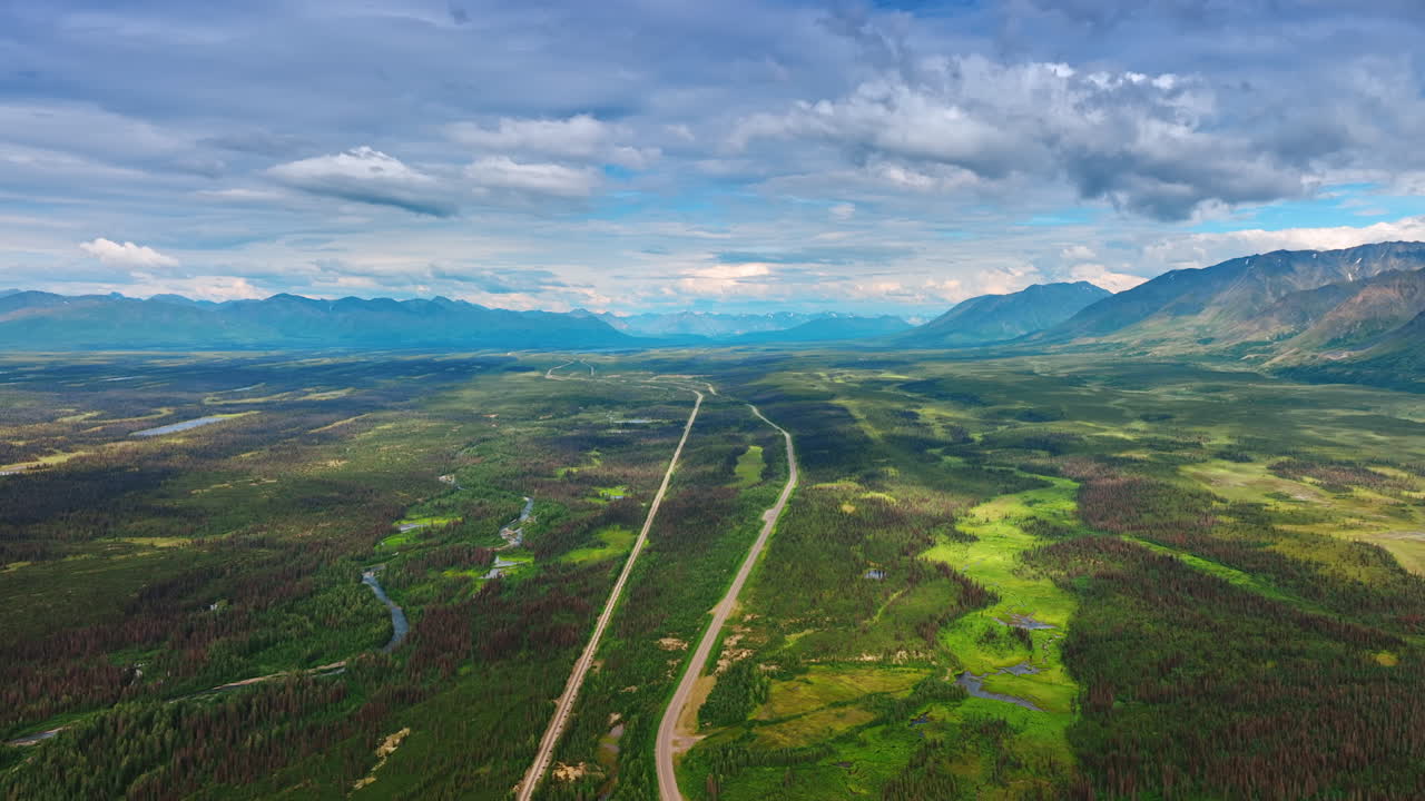 Panoramic View of Highway and Railway Across Tundra. An ultra-wide elevated vista shows a lonely highway and parallel railway line crossing vast, dark green Alaskan tundra