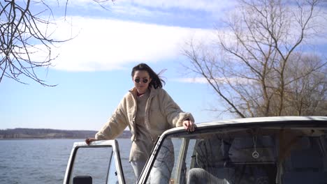 una joven hermosa morena con gafas de sol mira por la ventana de una camioneta junto a un lago.