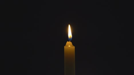 a single white candle burning. looping for use as a background or illustration of remembrance or celebration. the wind tries to put out the flame, but it recovers each time. the eternal flame.