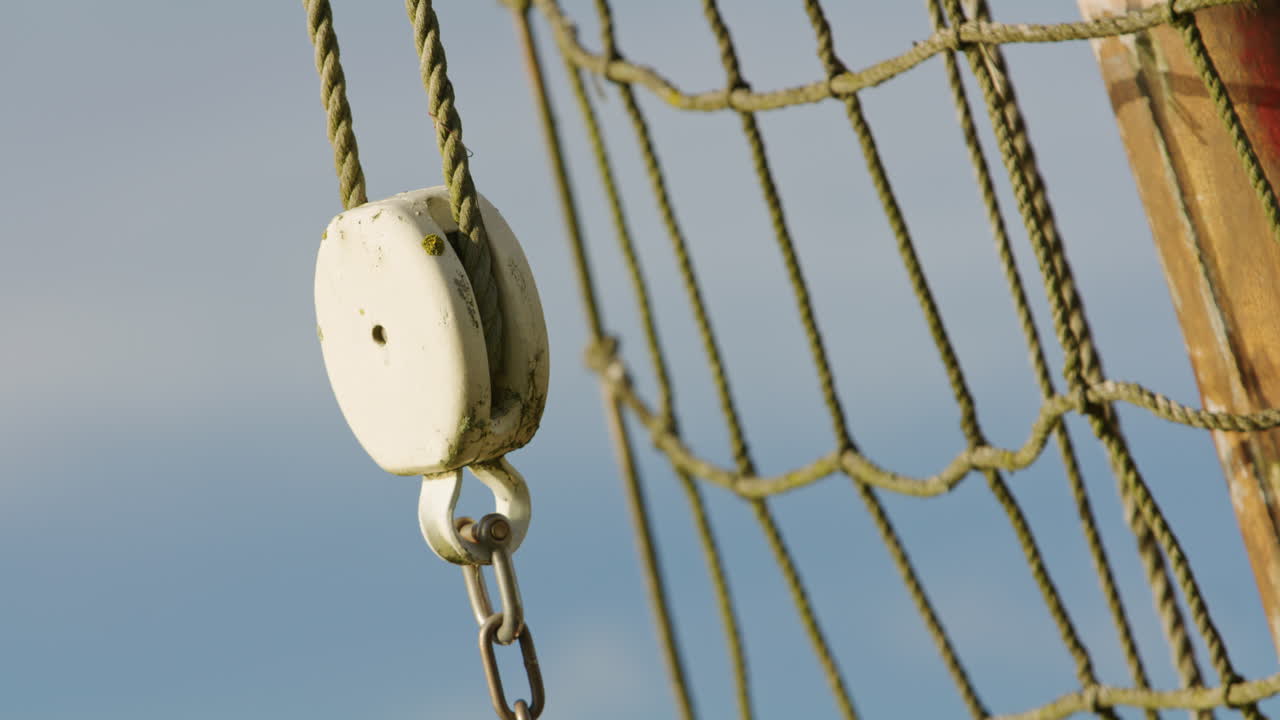 Primo piano di una carrucola marittima con rete di corda e catena su un cielo limpido, a simboleggiare connessione, stabilità, navigazione e artigianato nautico tradizionale.