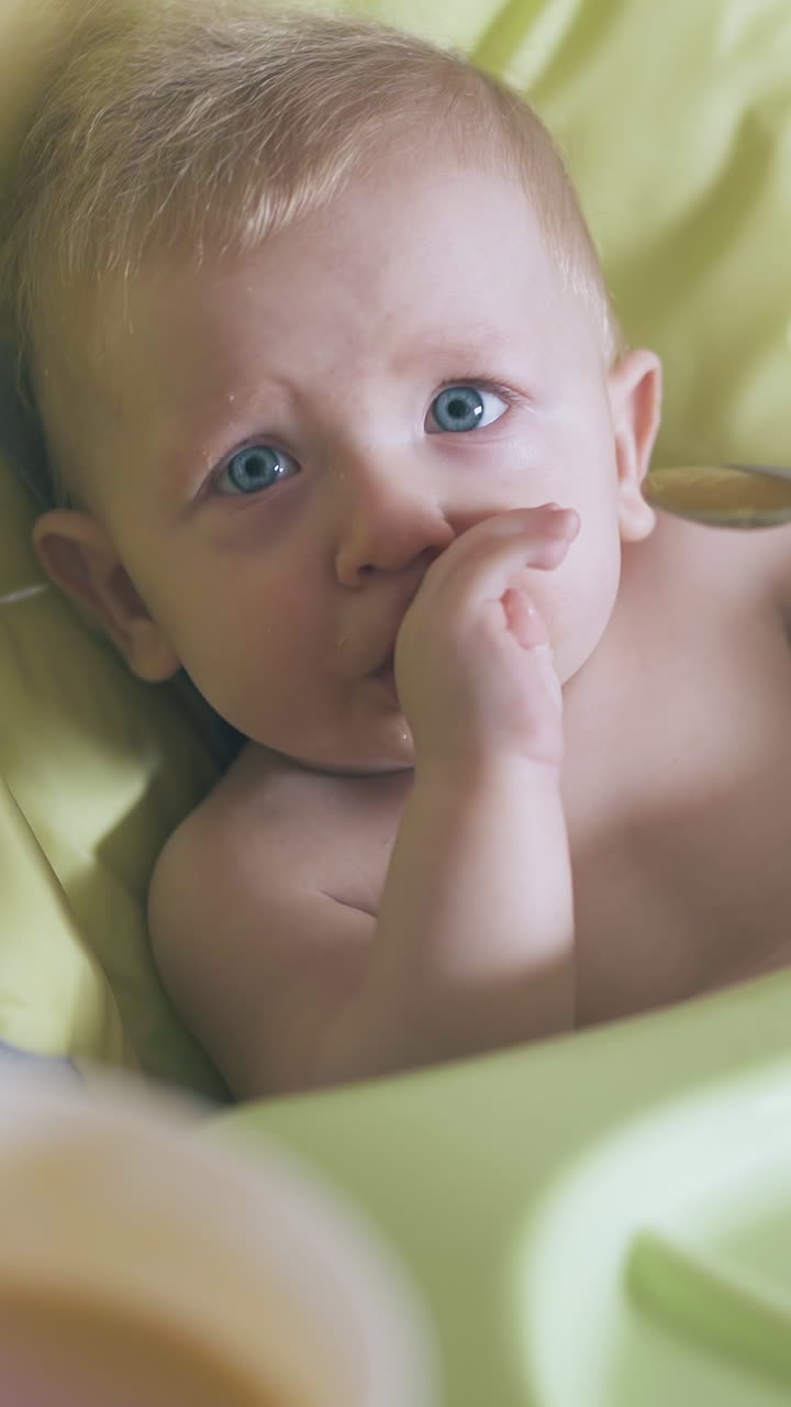 mother waits with spoon for baby to open mouth feeding cute son with fresh cream soup in highchair extreme close view