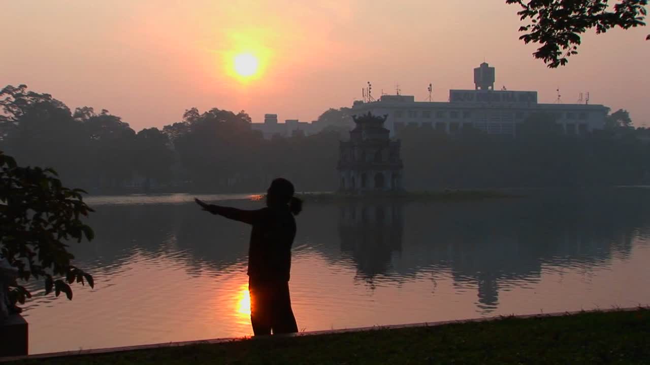 한 여성이 베트남 하노이의 호수 앞에서 태극권을 연습합니다.