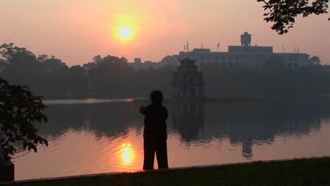 a woman practices tai chi in front of a lake in hanoi vietnam