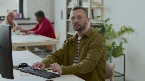 portrait of businessman in earbuds sitting at desk with computer in office