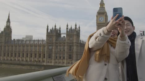 joven pareja asiática de vacaciones posando para selfie frente a las casas del parlamento en londres, reino unido 3