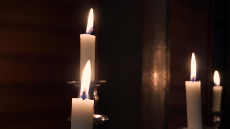 mid handheld shot of a few candles on a silver candlestick with wooden walls and a mirror in the background