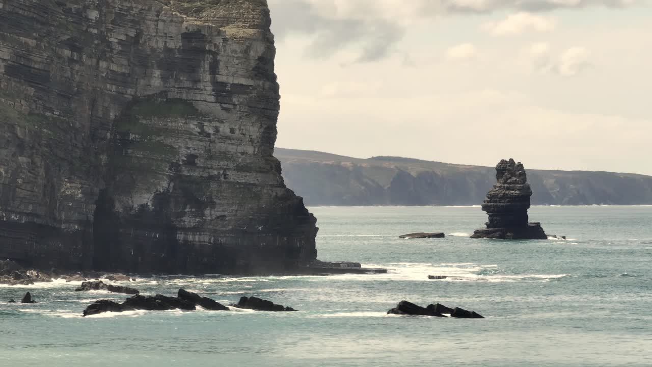Aerial shot flying over quiet waters along a coastline with cliffs and rocks on a cloudy day