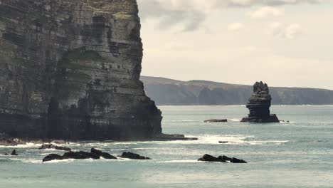 Aerial-shot-flying-over-quiet-waters-along-a-coastline-with-cliffs-and-rocks-on-a-cloudy-day