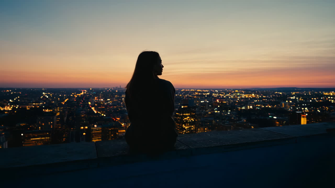 Woman Silhouetted Against a City Sunset from a Rooftop