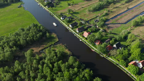 Vista-Aérea-De-Un-Barco-Navegando-En-El-Río-Con-Villas-Frente-Al-Mar-En-Ossenzijl-En-Frisia,-Países-Bajos