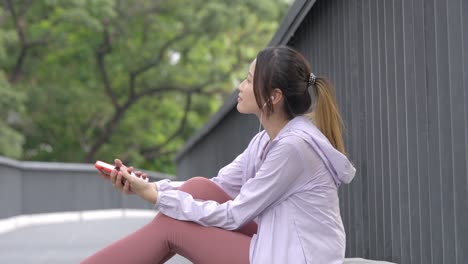 4k young asian woman listening to music from earphones and smartphone while jogging at public park the city in the morning.