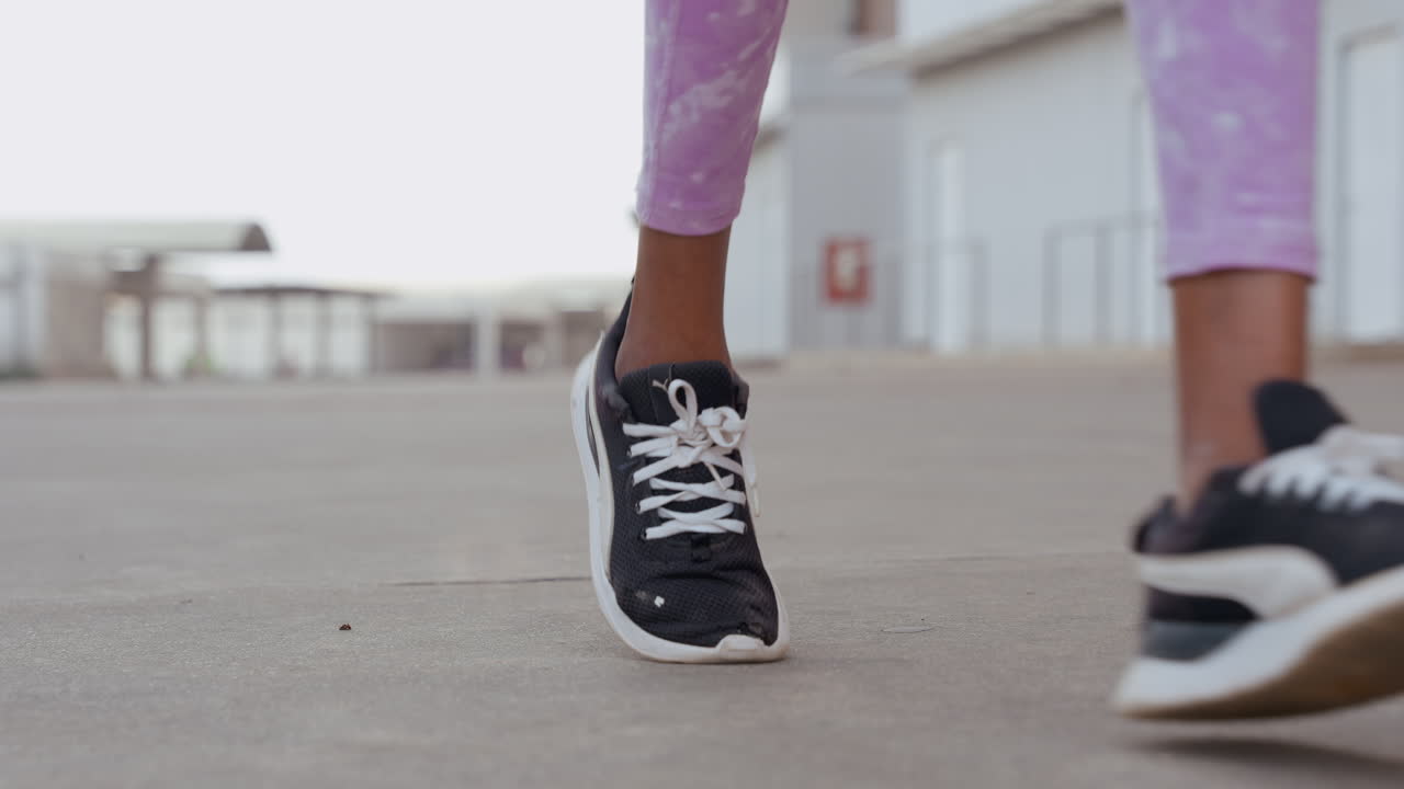 Primo piano di leggings viola che mostra le gambe e le scarpe da ginnastica di una runner nera su cemento di un tetto urbano, cadenza concentrata, passo costante, sessione di allenamento mattutina, sfondo industriale minimalista, atmosfera fitness grintosa.