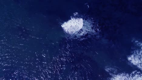 blue ocean water with rocks visible below, top down drone shot