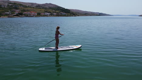 cámara lenta aérea de una turista en una tabla de remo en el mar adriático en la costa de la isla de pag en un día de verano