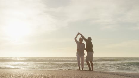 feliz pareja de graduados hispanos bailando en la playa al atardecer