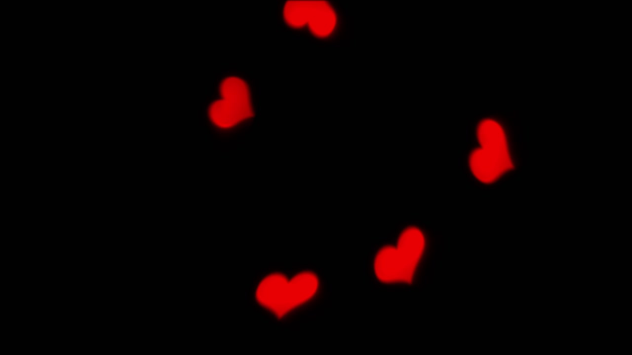 Romantic background of soft, out-of-focus red heart-shaped bokeh lights falling against black screen. For Valentine's Day or weddings