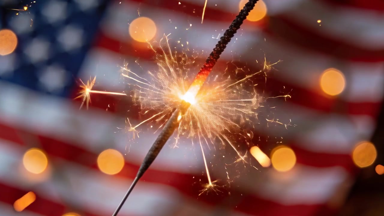 Lighting sparkler emitting sparks and embers for patriotism in front of American flag, warm lights