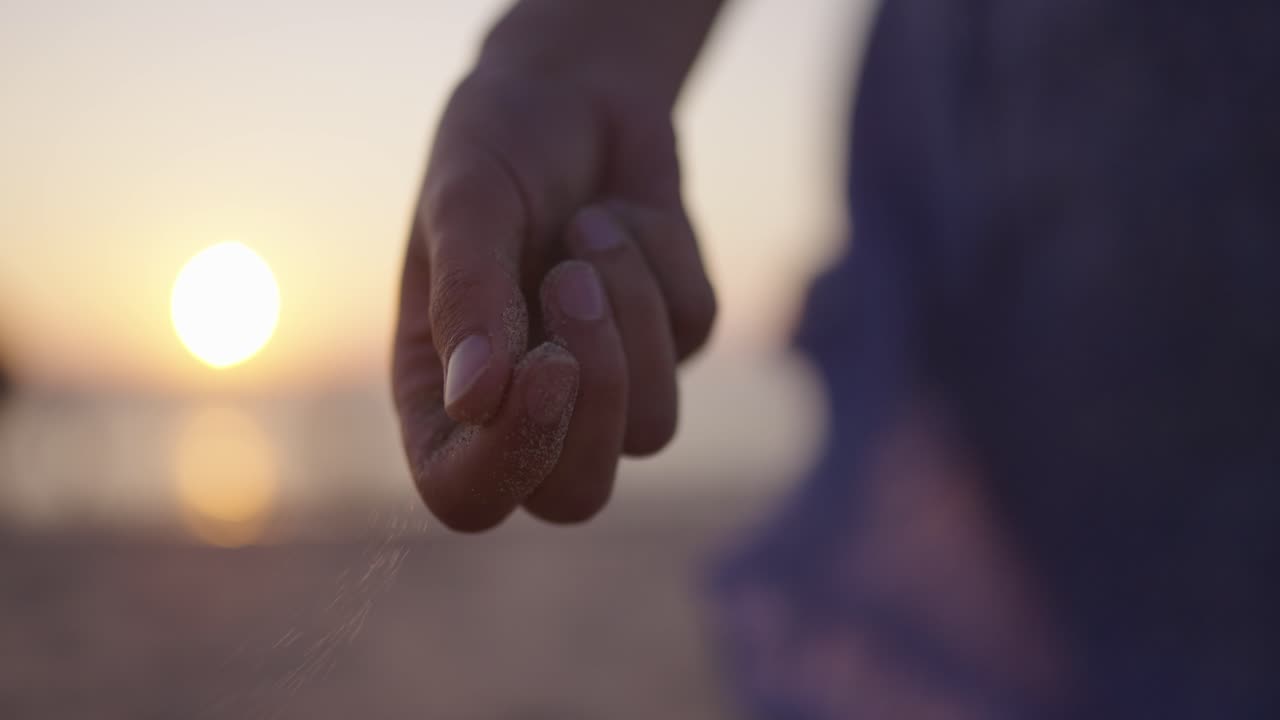 Sand slowly falls out of woman's hand, flowing dress