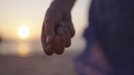 Sand-slowly-falls-out-of-woman's-hand,-flowing-dress