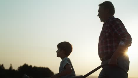 video of grandfather driving grandson in wheelbarrows at sunset