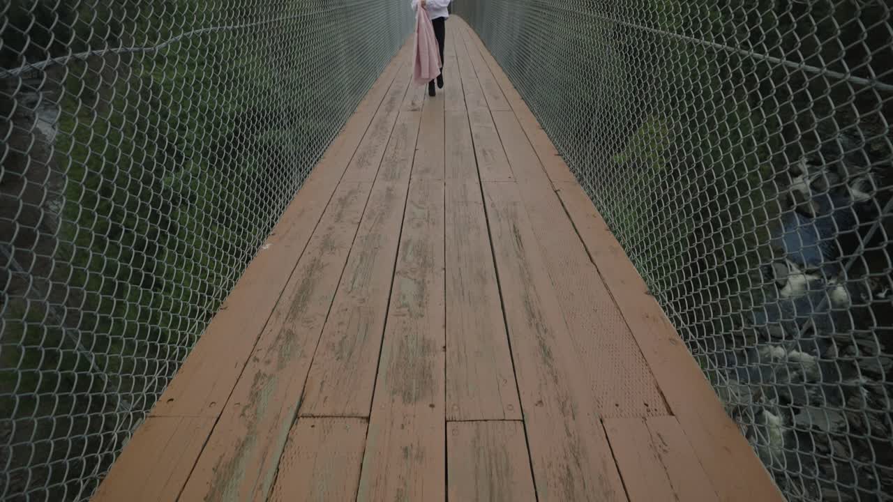 젊은 여성은 코티쿠크, 동부 타운십, 퀘벡 캐나다, 틸트업, 전신 샷, 슬로우 모션에 있는 현수교를 가로질러 걸어갑니다.