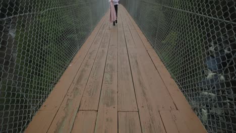 mujer joven camina a través de un puente peatonal suspendido en coaticook, municipios del este, quebec, canadá, inclinación hacia arriba, tiro de cuerpo completo, cámara lenta