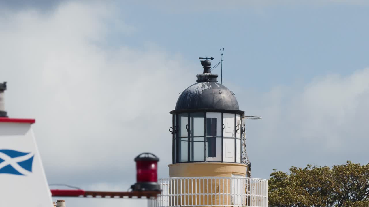 Camera slowly pans across Cromarty lighthouse, Scottish flag, and maritime beacon under daylight