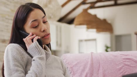 biracial woman sitting and talking on smartphone in living room