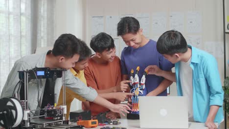 group of young asian boys with a laptop and 3d printing smiling to the camera while discussing about a cyborg hand at home