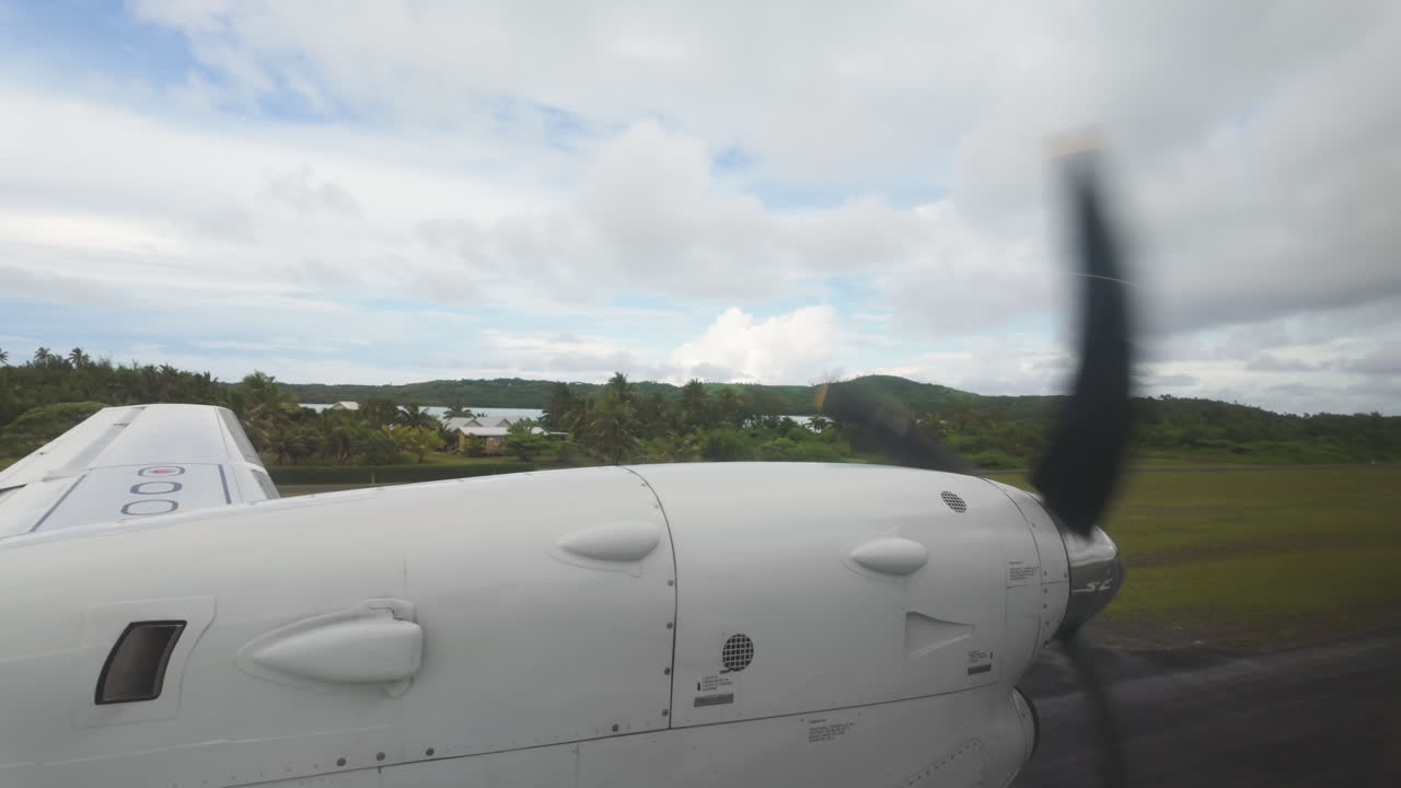 Plane descends, slow motion view from inside airplane looking out at wing and propellor over tropical islands