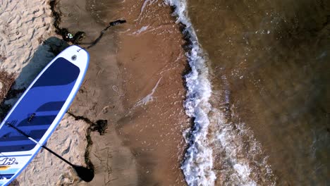 Top-down-clip-of-a-SUP-surfboard-on-the-waves-next-to-a-beautiful-tropical-beach