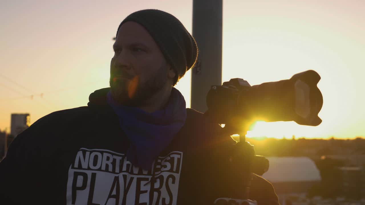 Man taking photos with DSLR camera of city landscape during setting sun with orange sky over horizon
