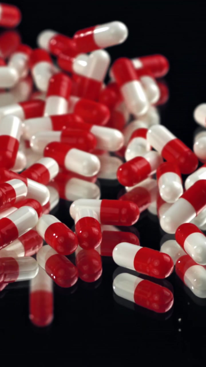 Red and White Capsules Falling onto a Black Reflective Surface