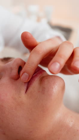 adult woman receiving professional lip cream application in cosmetology clinic by beautician