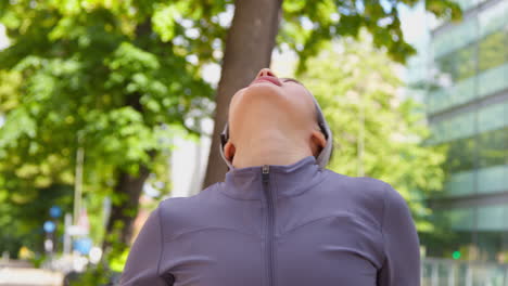 Close-Up-Front-View-Of-Young-Woman-Exercising-Running-Along-City-Street-Wearing-Wireless-Earbuds-Resting