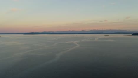 gradual pan right reveals silhouette of pacific coast mountain range in distance as drone flies above puget sound in washington state, aerial
