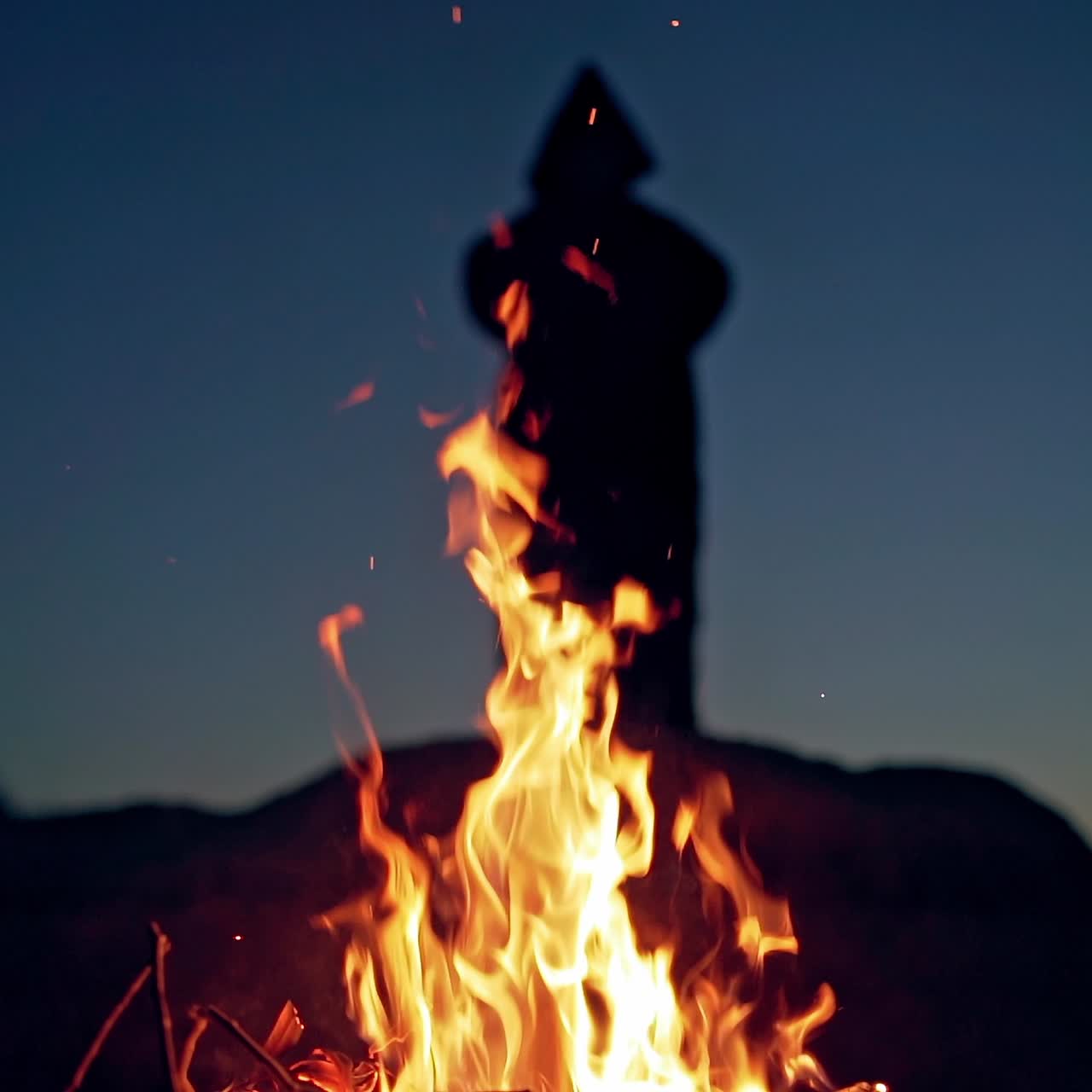 Shamanism over the fire at night. Evil figure in black mantle. Bright flame of fire on the background of dark silhouette of death. Halloween concept.